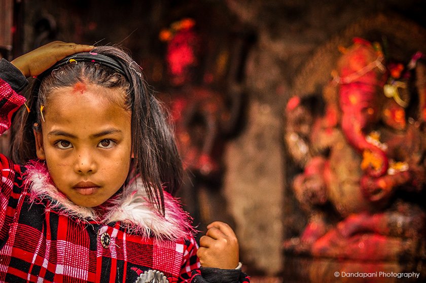 A young girl places blessed flower petals in her hair after worshipping Ganesha at a roadside shrine in Kathmandu, Nepal.